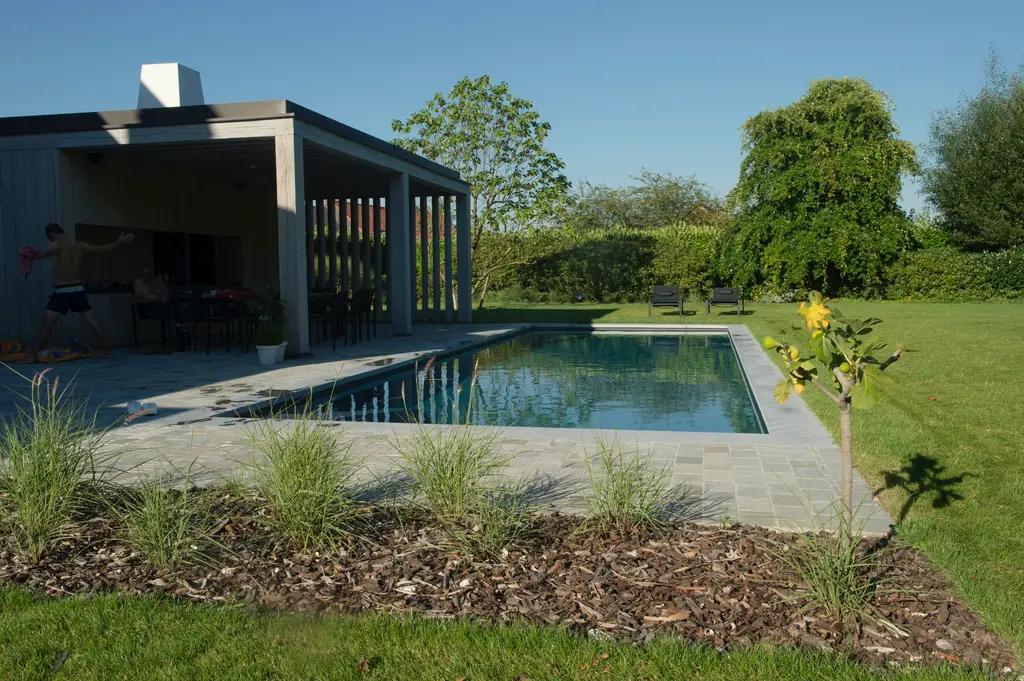 Zwembad met natuurstenen rand, poolhouse met houten lamellen en siergrassen — Elegante tuin met zwembad, Meise