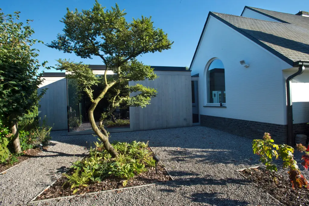 Grindvlak met gesnoeide boom en beplanting tussen witte woning en houten scherm — Elegante tuin met zwembad, Meise
