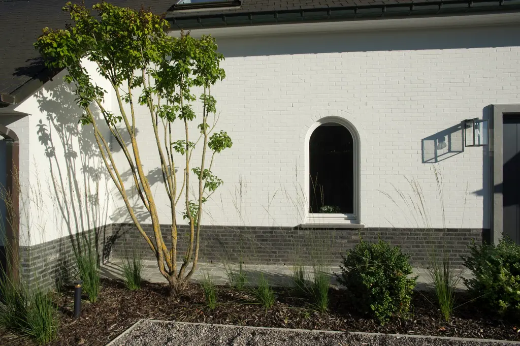 Meerstammige heester tegen de witte gevel met boogvenster, met lage beplanting — Elegante tuin met zwembad, Meise