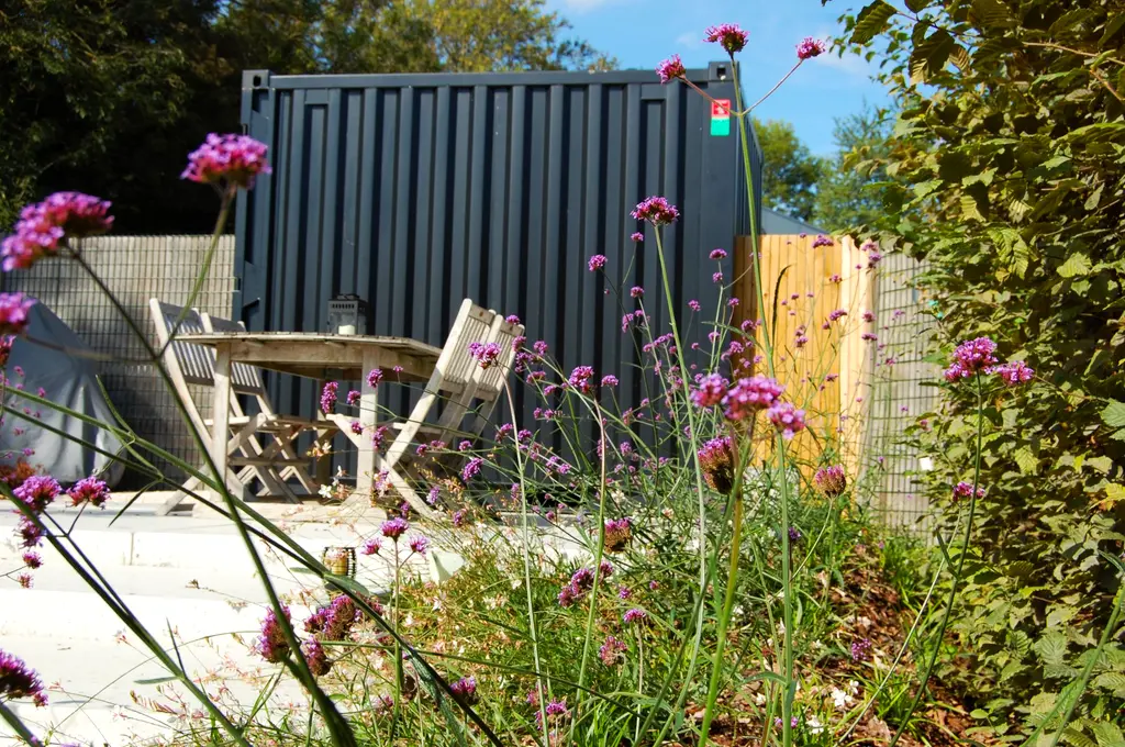 Bistrotafel met twee stoelen bij een zwarte zeecontainer, paarse bloemen vooraan — Gezellige kleine stadstuin, Halle