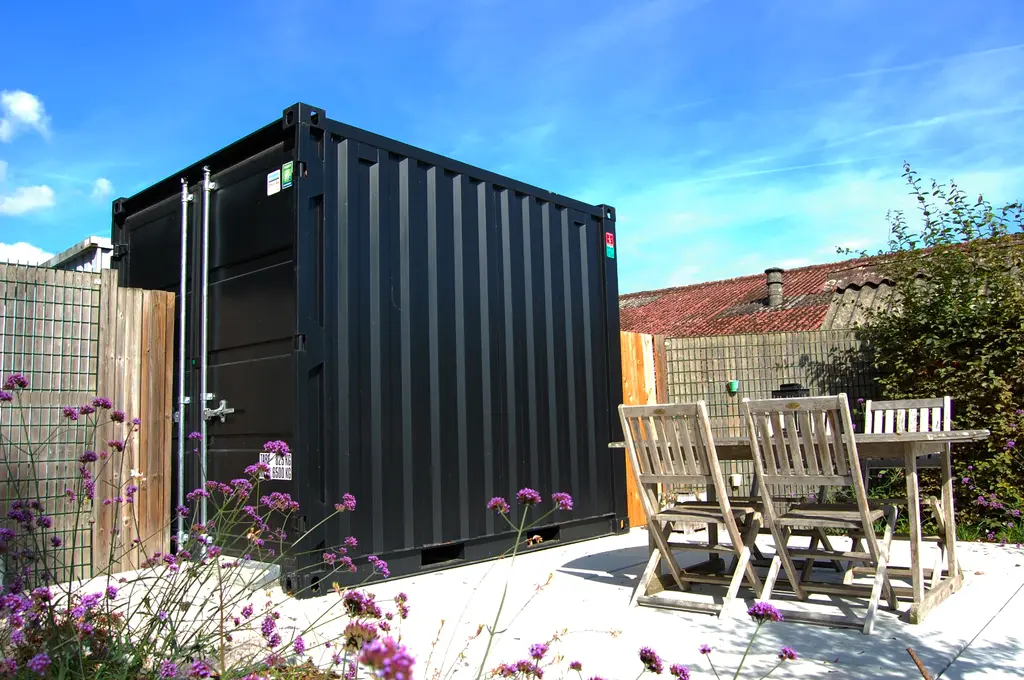 Zwarte zeecontainer op licht terras met houten tuintafel en stoelen — Gezellige kleine stadstuin, Halle