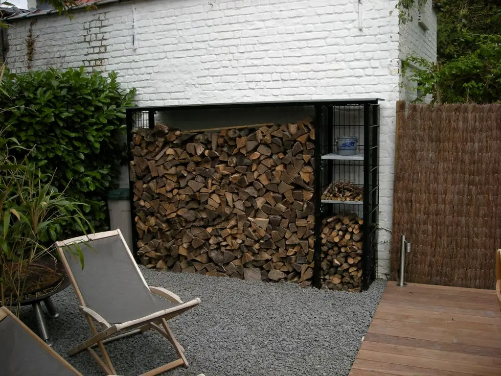 Houtopslag in stalen rek tegen witte muur, strandstoel op grind en houten vlonder — Gezellige stadstuin, Ukkel