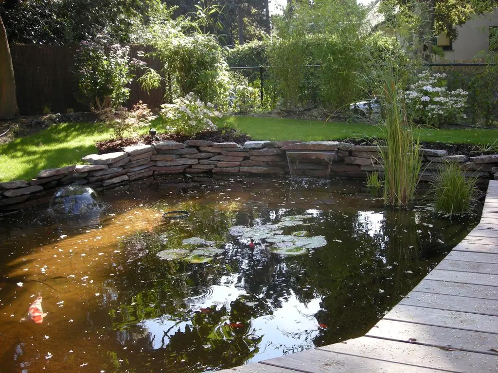 Vijver met waterlelies en fontein, natuurstenen stapelmuur en houten vlonder langs de rand — Gezellige stadstuin, Ukkel