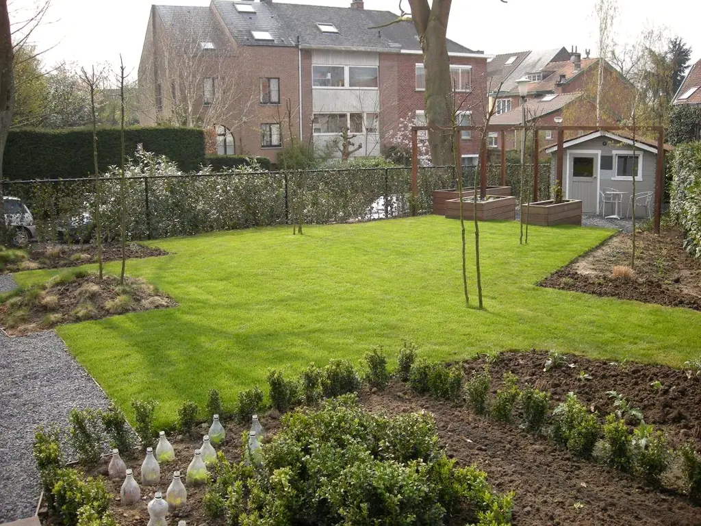 Pas aangelegd gazon met plantvakken en jonge heesters, tuinhuis achteraan — Gezellige stadstuin, Ukkel
