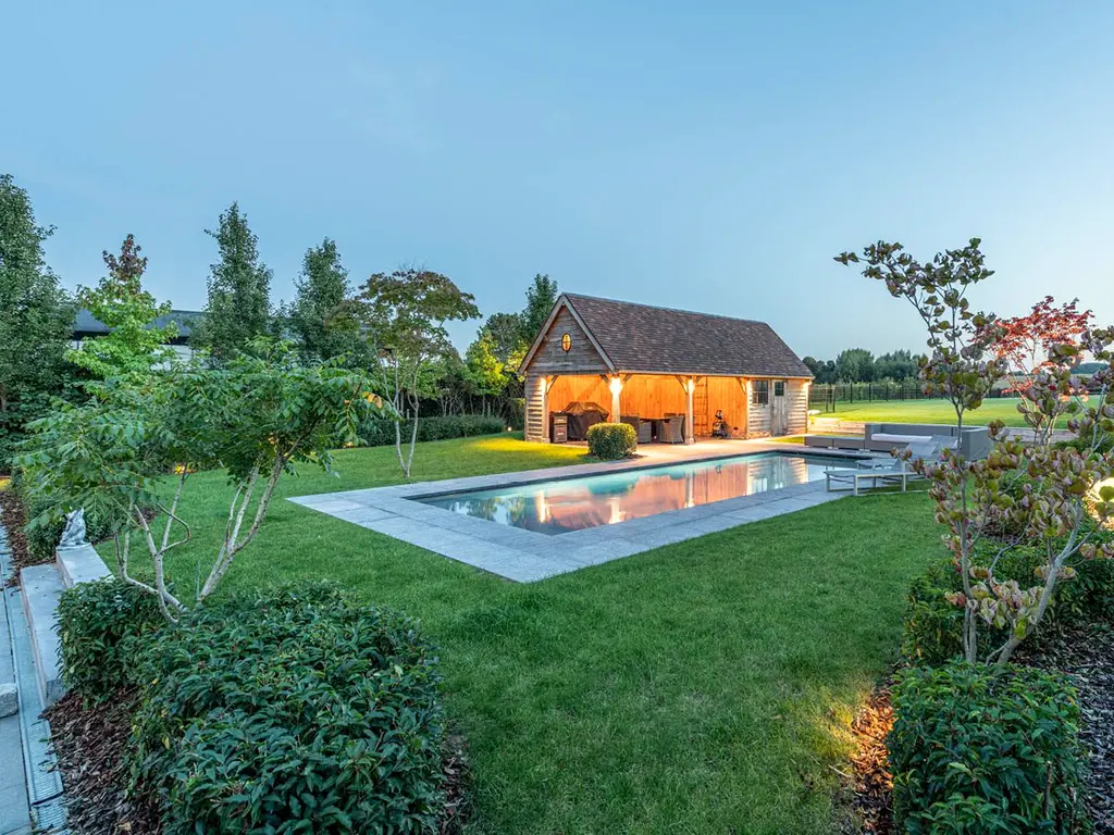 Verlicht zwembad en poolhouse in de schemering, omringd door gazon en borders — Klassieke tuin met zwembad, Roosdaal