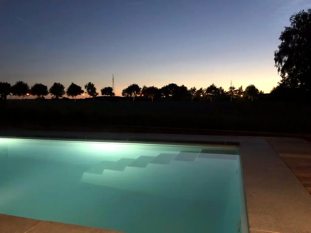 Verlicht zwembad met trap bij zonsondergang, met bomenrij aan de horizon — Klein en krachtig, Relegem