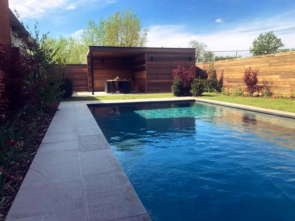 Zwembad met lichte stenen rand naar houten poolhouse, houten schutting en gazon — Oase-tuin, Ternat