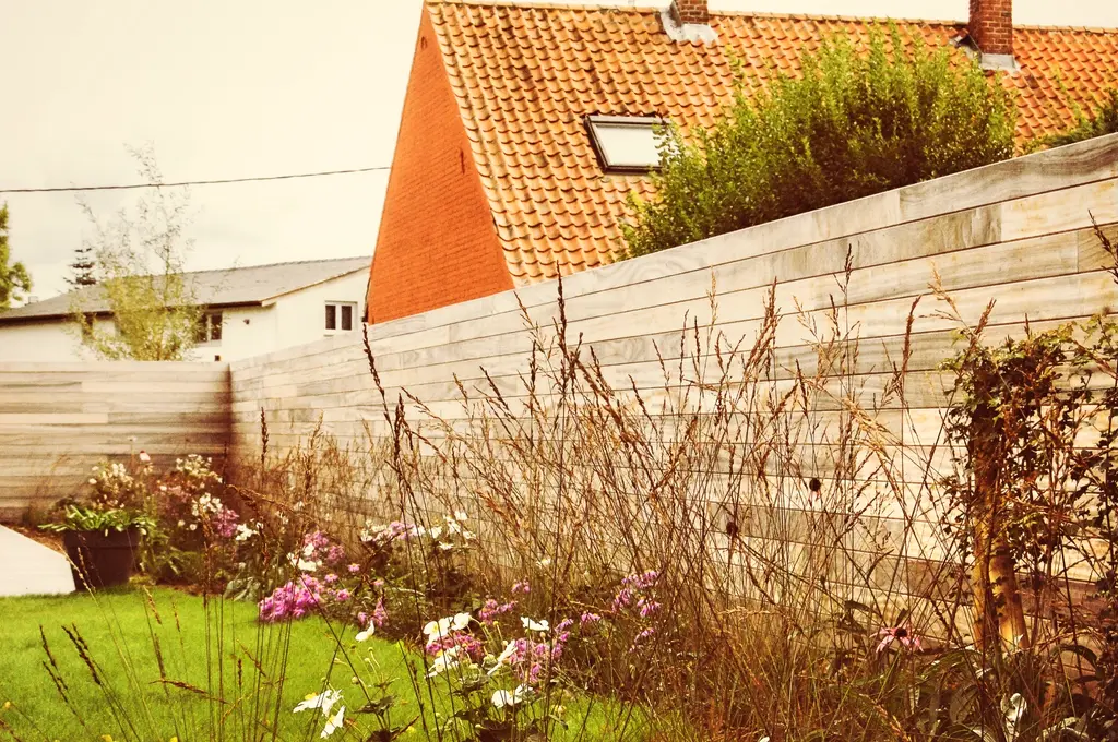 Border met siergrassen en roze bloemen langs een houten schutting — Open en toch gezellig