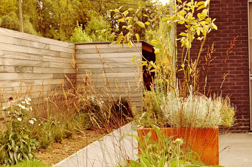 Cortenstalen plantenbak met wit bloeiende planten en grassen langs houten schutting — Open en toch gezellig