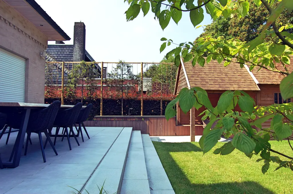 Licht terras met brede treden naar het gazon, buitentafel en houten bijgebouw