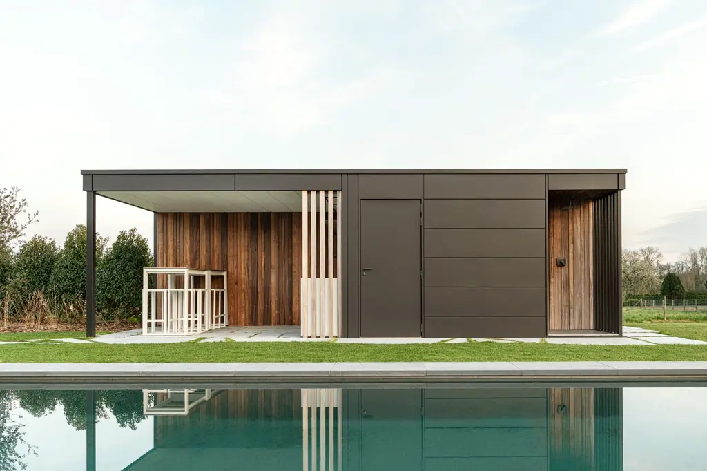 Modern poolhouse met donkere gevel en houten lamellen, weerspiegeld in het zwembad