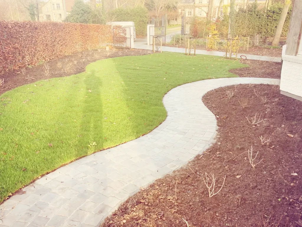 Gebogen pad van lichte kasseien tussen pas aangeplante borders en gazon — Romantische tuin met zwembad, Asse