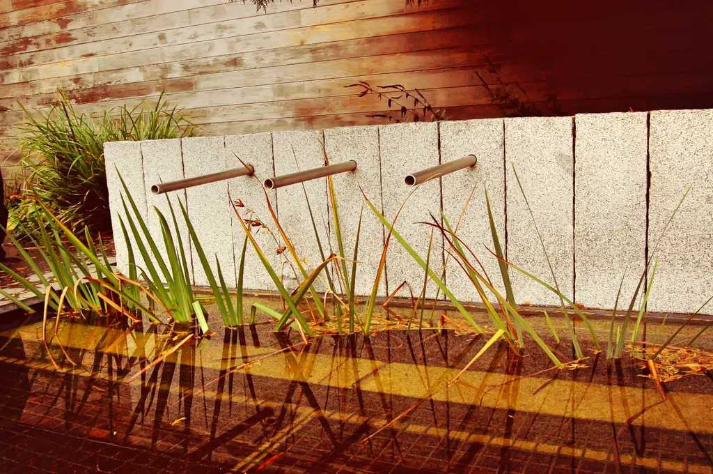 Waterwand van natuursteen met drie metalen spuwers boven een bak met waterplanten — Smeltkroes van stijlen, Dilbeek