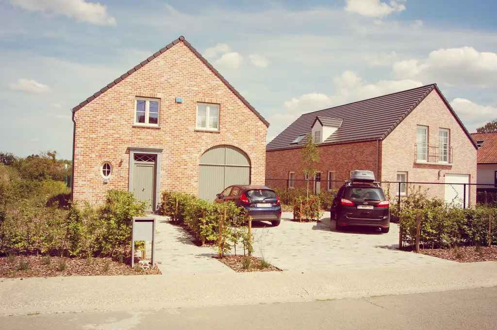 Voortuin met oprit en jonge hagen bij twee bakstenen woningen — Spelen en genieten, Beersel