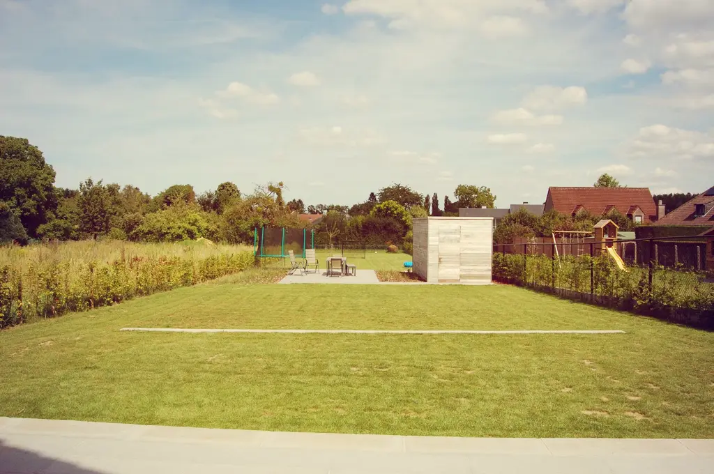 Diepe tuin met lang gazon, terras, houten berging en speeltoestel — Spelen en genieten, Beersel