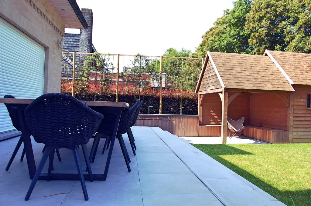Terras met tuintafel, houten bijgebouw met overkapping en leibomen — Uitnodigende tuin met buitenkeuken, Asse