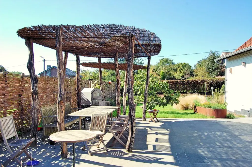 Terras met houten tuinmeubels onder een pergola van ruwe boomstammen — Wilde eetbare tuin, Sint-Pieters-Leeuw